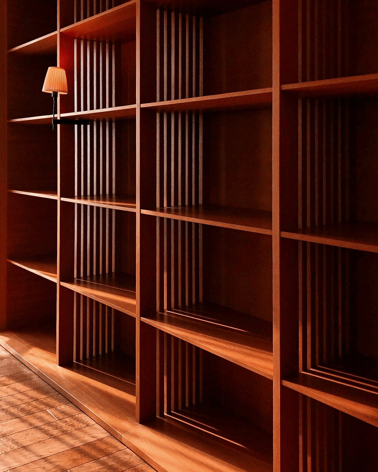 Une bibliothèque en bois sombre à claire-voie, dans la lumière du soir