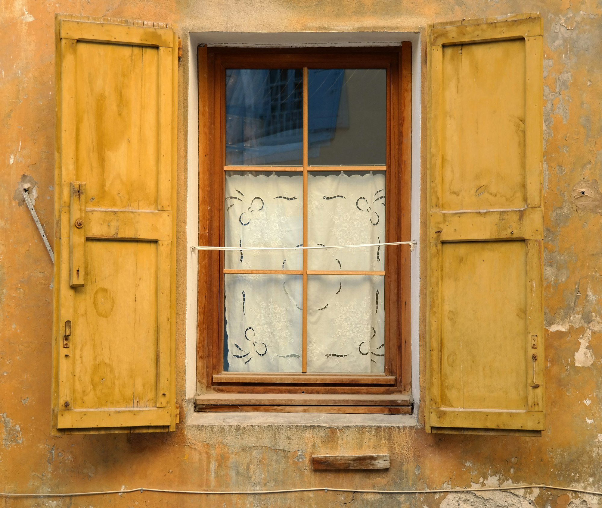 Une fenêtre à petits bois et ses volets ouverts, sur une façade ancienne